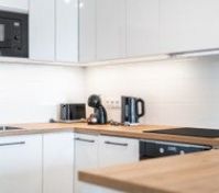 A modern, fully equipped kitchen with sleek white cabinets, wooden countertops, and essential appliances. Stylish, bright, and perfect for cooking and dining.